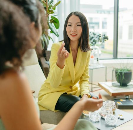Asian nutritionist in a yellow blazer advising a client on healthy supplements indoors.